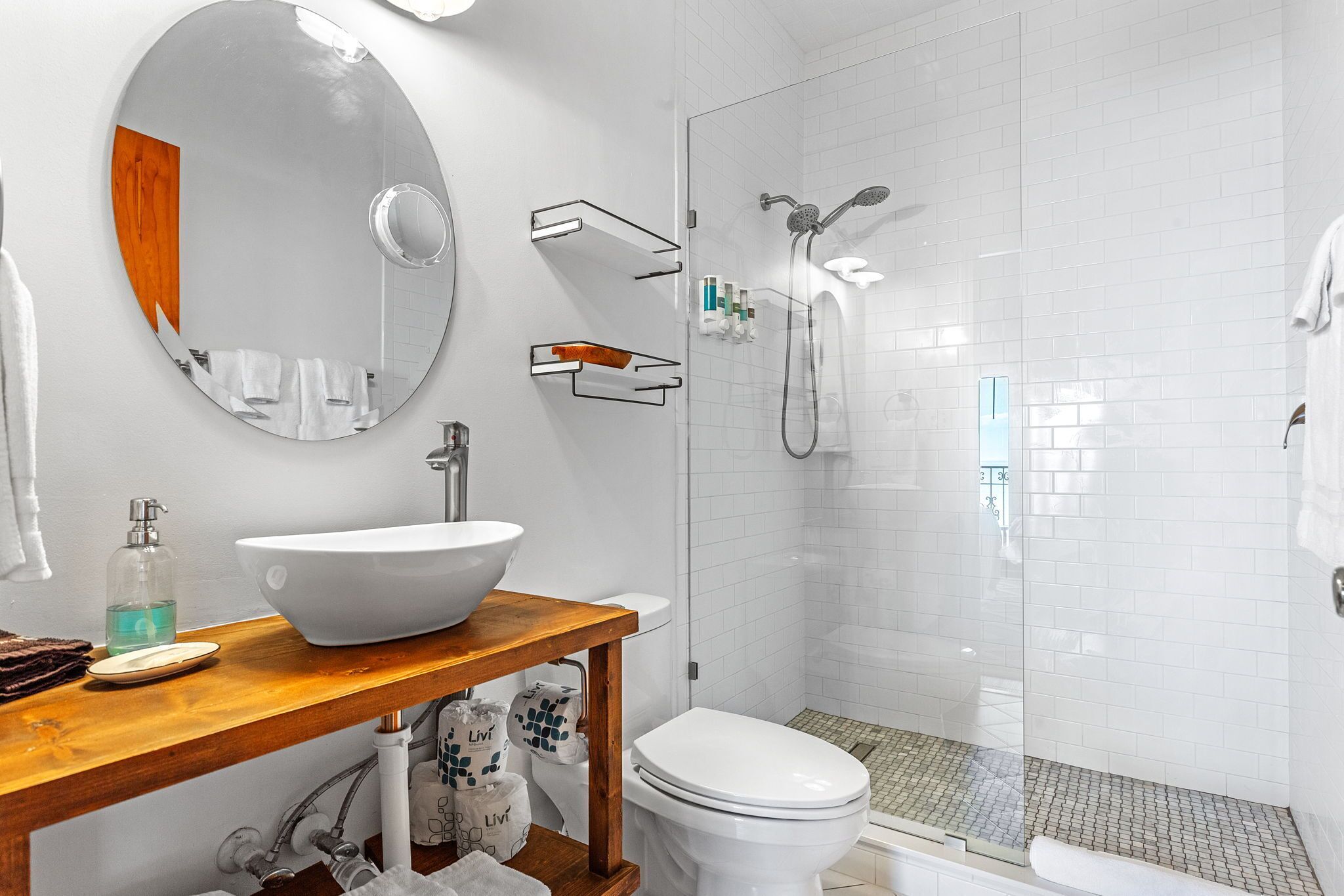 Ein modernes Badezimmer mit einem großen, ovalen Spiegel, einem weißen Waschbecken, einer Toilette und einer Duschkabine.