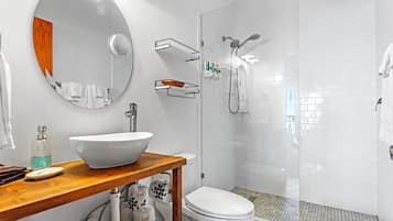 Ein modernes Badezimmer mit einem großen, ovalen Spiegel, einem weißen Waschbecken, einer Toilette und einer Duschkabine.