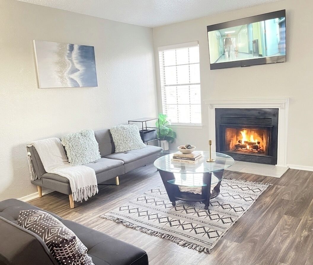 A living room with a fireplace, a sofa, a coffee table, and a television mounted on the wall.