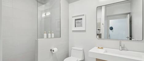 A modern bathroom with a glass-enclosed shower, a white toilet, a sink with a mirror, and a framed inspirational quote on the wall.