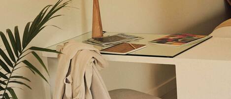 A small, neatly arranged workspace with a glass table, a lamp, a chair, and a potted plant.