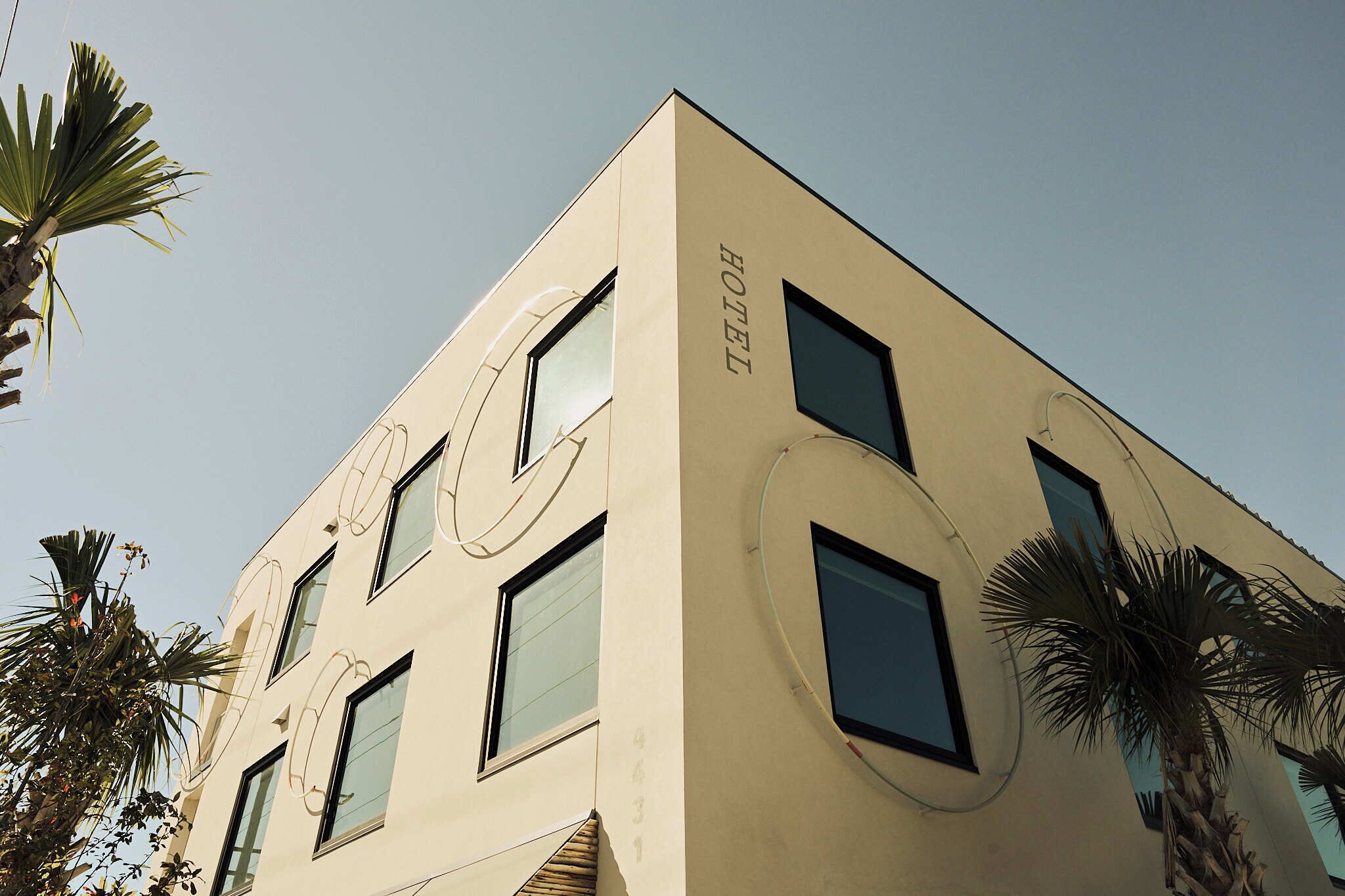 A modern hotel building with a beige facade, multiple windows, and a prominent "HOTEL" sign on the side.