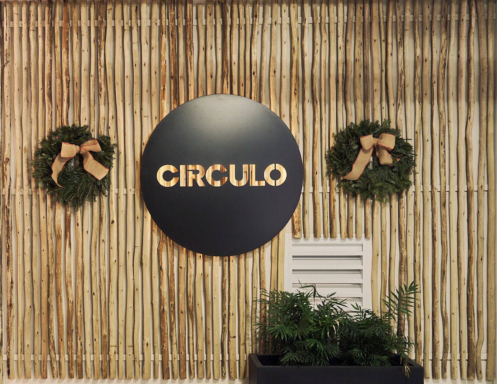 Una pared con listones de madera verticales, un letrero circular con la palabra "CIRCULO" en el centro, y dos coronas a cada lado.