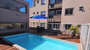 A rooftop pool with wooden decking, a blue umbrella, and outdoor furniture. - Stay in a good location in the city center of Bombinhas. (Bombinhas)
