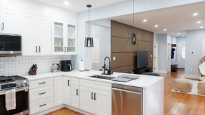Een moderne keuken met witte kasten, een inbouwoven, een vaatwasser en een groot keukenblok met een spoelbak.