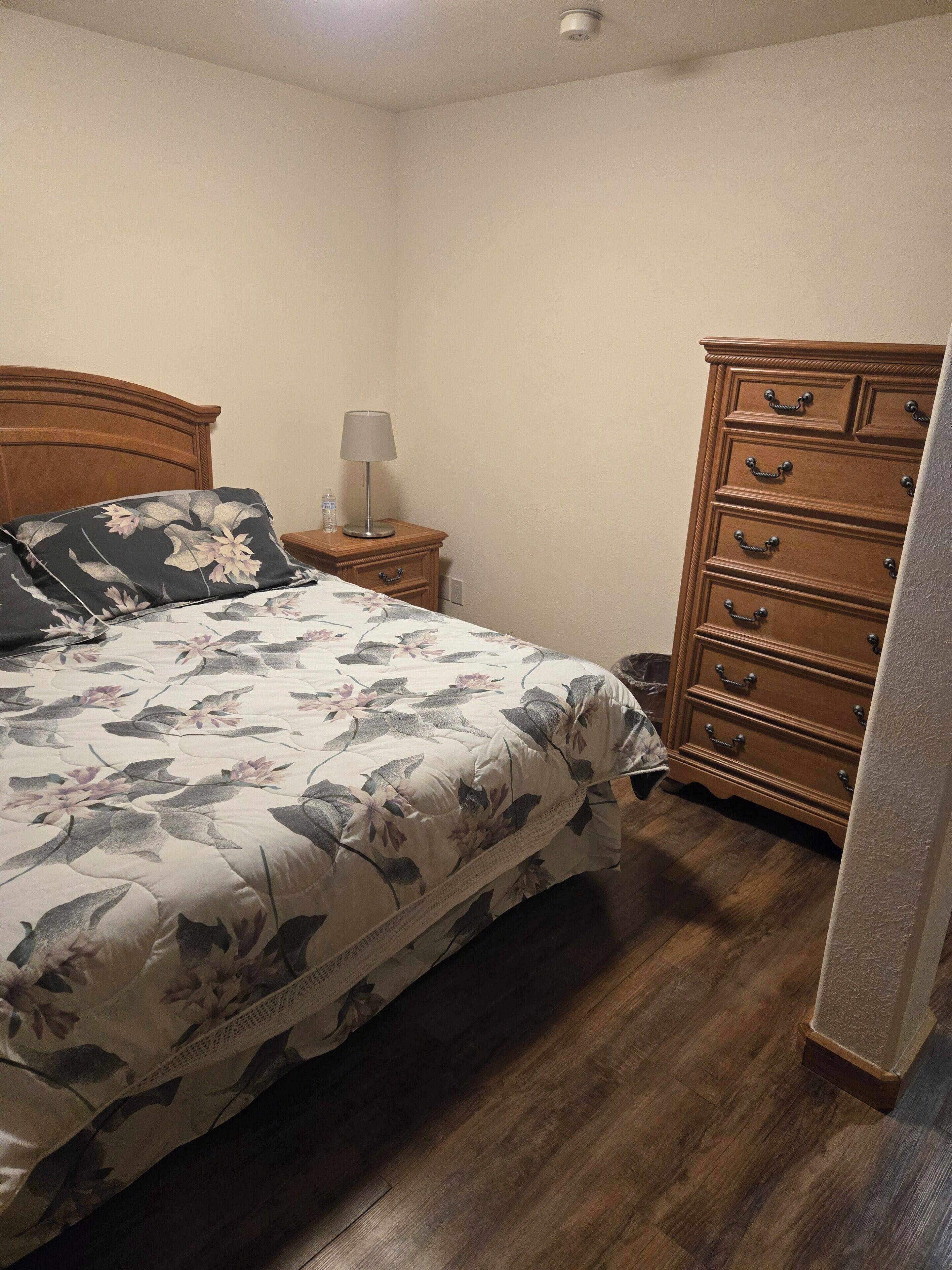 A bedroom with a wooden bed, a nightstand with a lamp, and a wooden dresser.