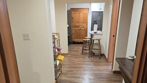 Käytävällä on puulattia, keittiöalueella kaappeja ja jääkaappi sekä oleskelualue, jossa on jakkaroita.