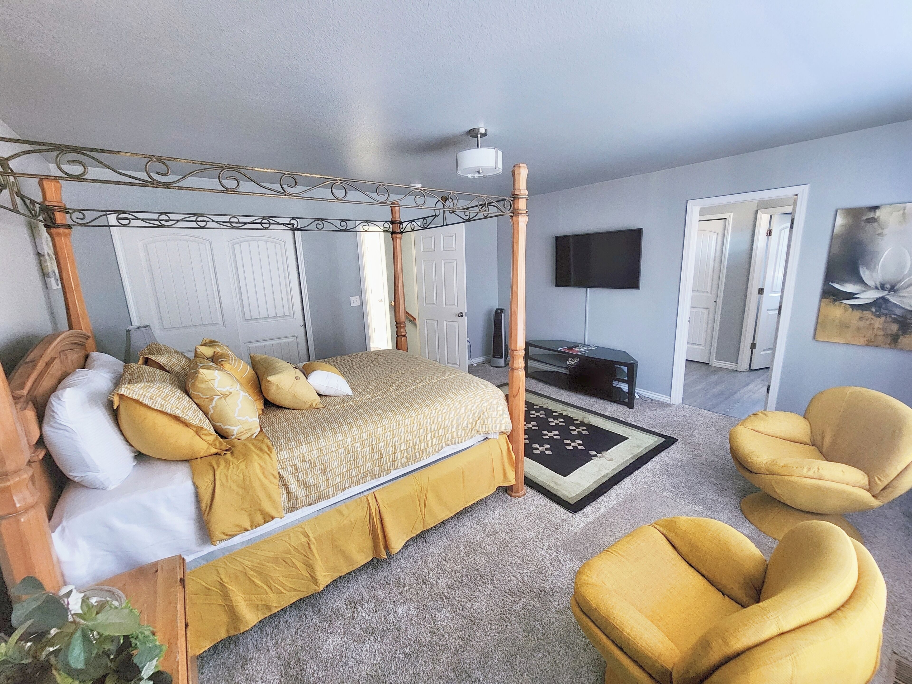 A four-poster bed with a canopy, a television mounted on the wall, and a large painting.