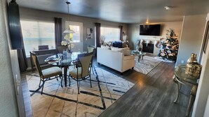 A modern living room with a sofa, coffee table, and a TV. There is a dining area with a table and chairs. A Christmas tree is visible in the background. - Modern Family Getaway with Mountain Views (Colorado Springs)