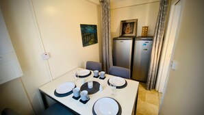 Un comedor con una mesa preparada para cuatro personas, dos refrigeradores al fondo y un cuadro en la pared.