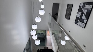 A modern interior with a staircase, glass railings, and pendant lighting.
