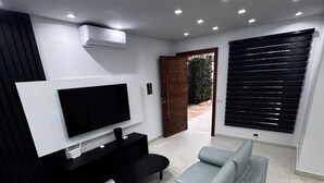 A modern living room with a flat-screen TV, a black entertainment unit, a light blue sofa, and a large window with blinds.