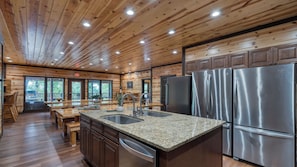 A kitchen with wooden paneling, stainless steel appliances, granite countertops, and a dining area with wooden furniture. - 16+ Guests Indoor Pool, Theater & Game Room in the Smokies Buckskin by Avantstay (Sevierville)