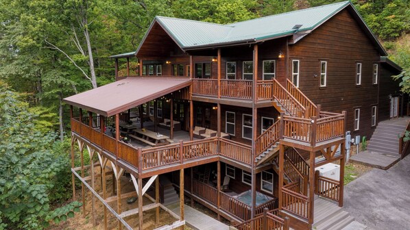 A multi-story wooden cabin with a balcony, outdoor seating, and a hot tub. - 16+ Guests Indoor Pool, Theater & Game Room in the Smokies Buckskin by Avantstay (Sevierville)