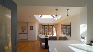 A spacious kitchen with a large island, a dining area with a table and chairs, and a view of the garden through the windows. - Cosy retreat in Devon, The Old Chapel (Feniton)