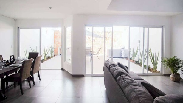 A spacious living area with a dining table and chairs, a sofa, and a sliding glass door leading to an outdoor patio.