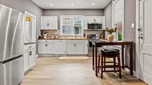 A modern kitchen with white cabinets, stainless steel appliances, and a wooden dining table with two stools.