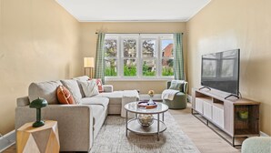 A living room with a sofa, coffee table, TV stand, and a window with curtains.
