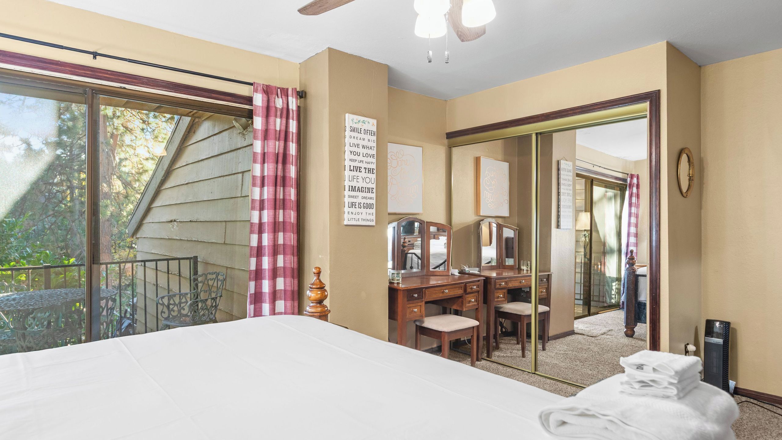 A bedroom with a large bed, a desk with a mirror, a dresser, and a balcony with a checkered curtain.