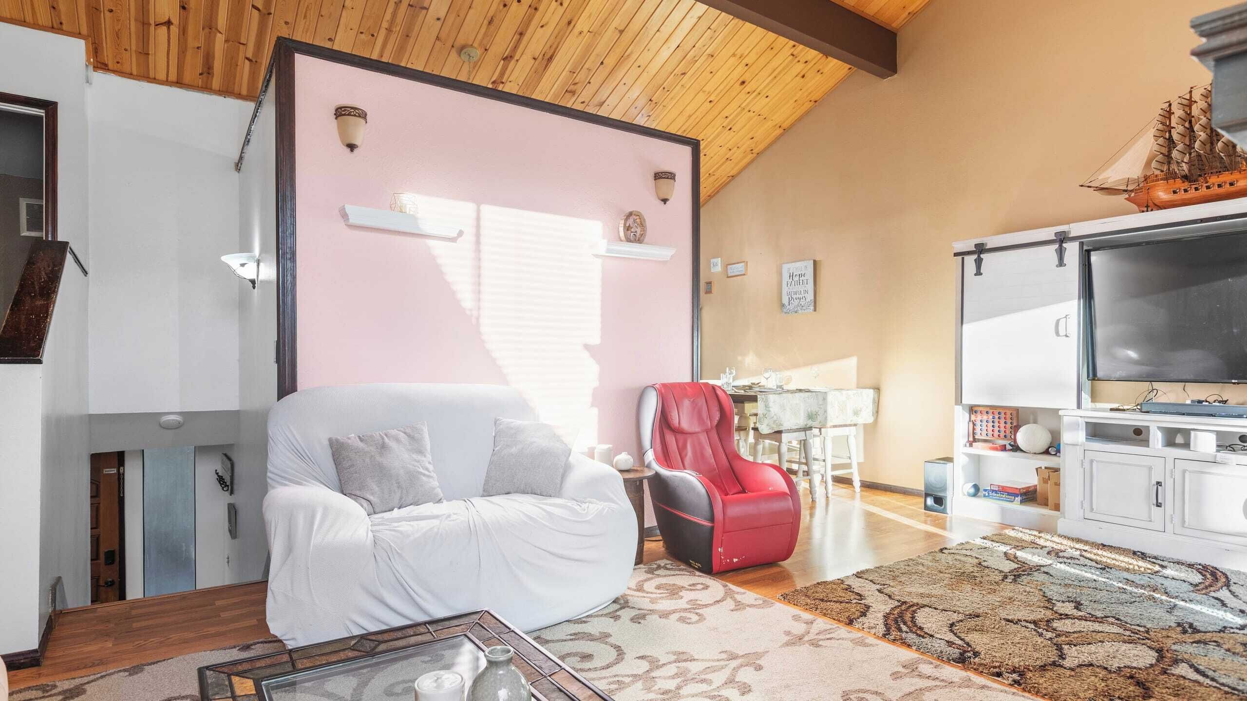 A living room with a white sofa, a red chair, a television, and a wooden ceiling.