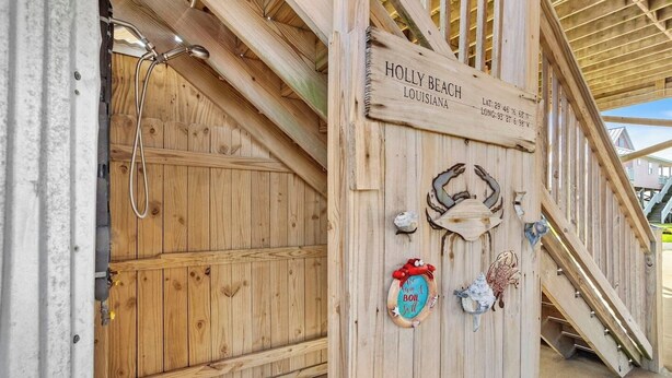Uma porta de madeira com uma placa que diz "HOLLY BEACH, LOUISIANA" e um lance de escadas de madeira que leva a um andar superior.