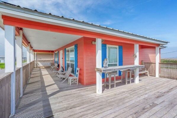 A wooden deck with a covered porch, outdoor seating, and a view of the beach.