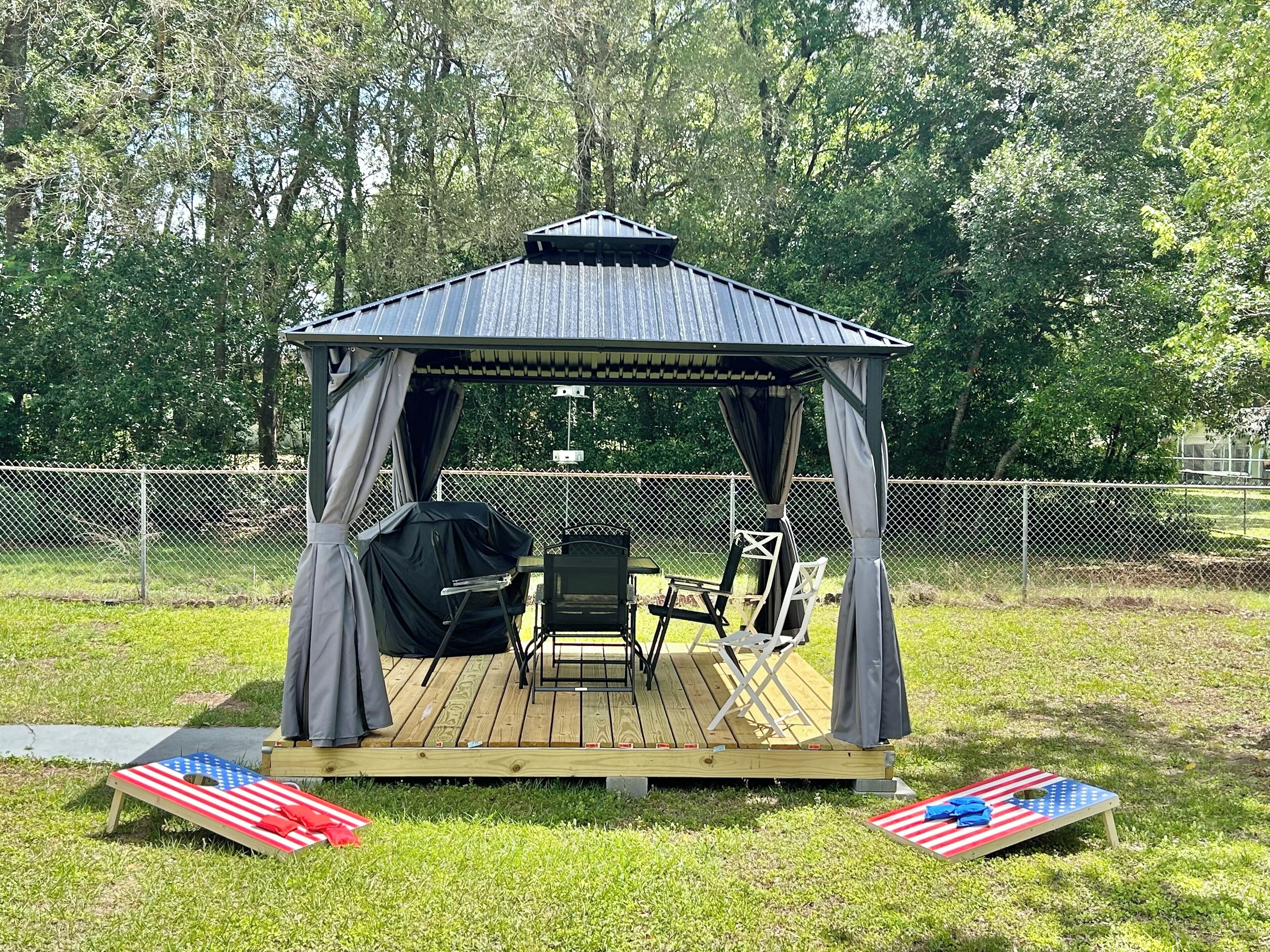 A gazebo with a metal roof and curtains, a grill, and folding chairs on a wooden deck.