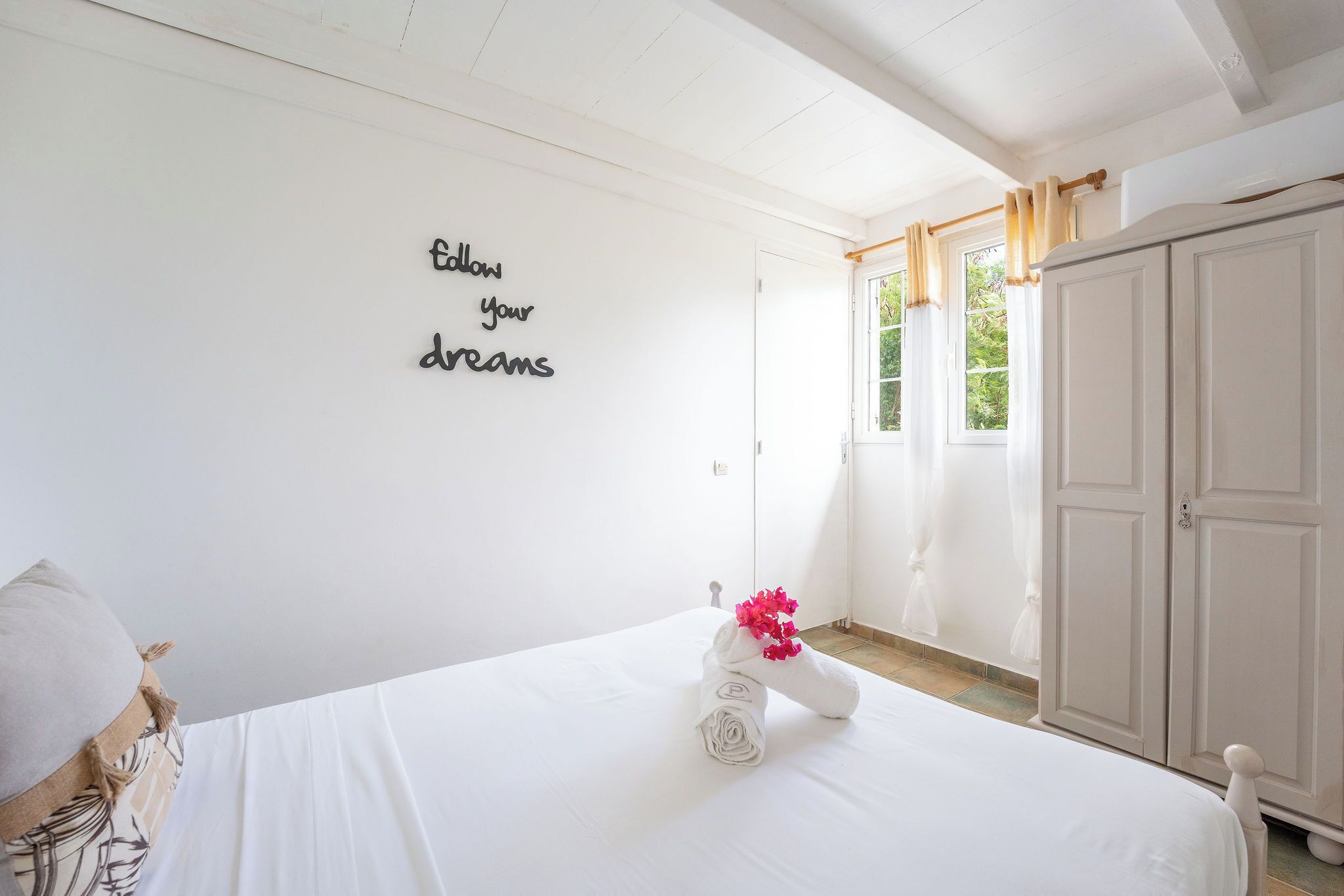 Una habitación de hotel con cama, un armario, cortinas en una ventana y una pared con una frase motivacional.