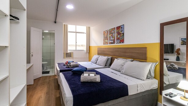 Une chambre d’hôtel avec deux lits, une salle de bain, une tête de lit en bois et des œuvres d’art accrochées au mur.
