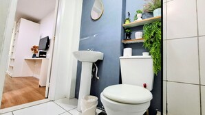 Une salle de bain équipée de toilettes, d’un lavabo, d’un miroir et d’étagères où sont posées des plantes.