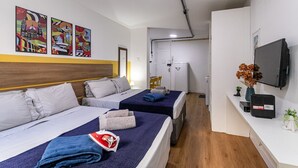 Une chambre d’hôtel avec deux lits, une télévision, un bureau, une chaise et des œuvres d’art accrochées au mur.