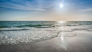 Una platja amb ones que brollen suaument a la riba sota un cel serè.