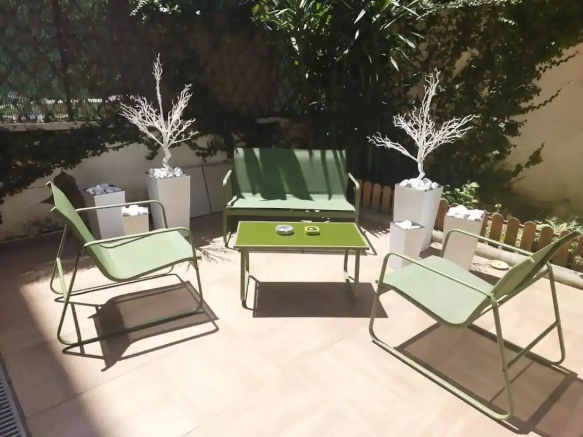 Une terrasse extérieure avec des chaises et une table en métal vert, entourée de plantes en pot.