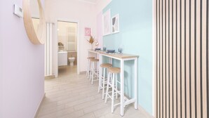 Um corredor estreito com um espelho emoldurado em madeira, uma porta branca que dá para um banheiro, e uma parede azul-claro com design em ripas de madeira.