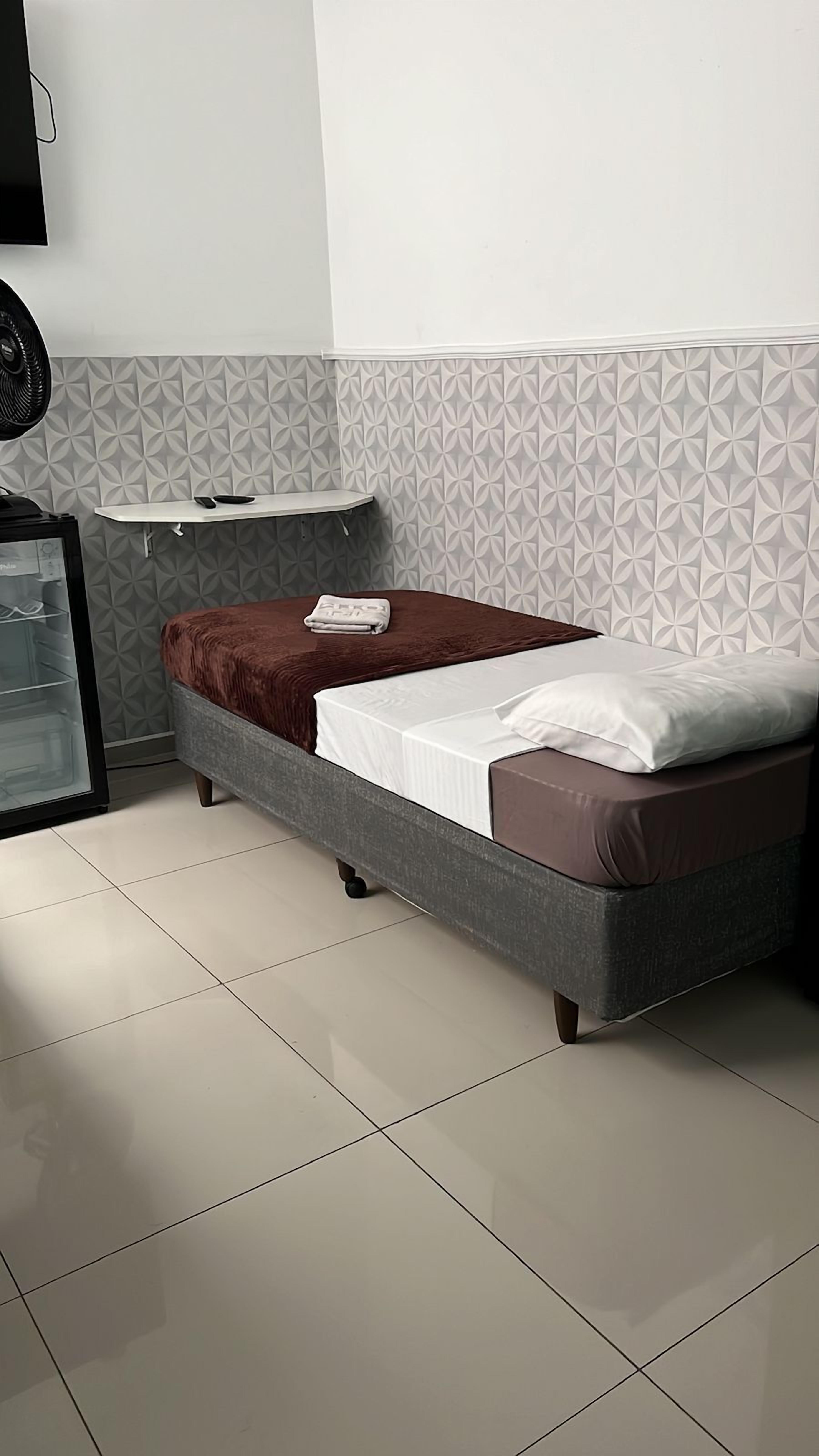 Ein modernes Schlafzimmer mit Bett, einem kleinen Tisch und einem Wandventilator.
