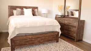 Een slaapkamer met een houten bed, nachtkastje, dressoir en spiegel.