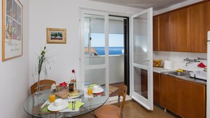 A dining area with a glass table, chairs, and a view of the sea through an open door. - One Bedroom Apartment with Loggia and Sea View (Dubrovnik)