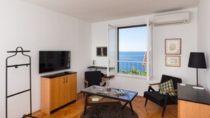 A modern living room with a large TV, a dining table, a sofa, and a view of the sea. - One Bedroom Apartment with Loggia and Sea View (Dubrovnik)