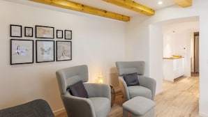 Un soggiorno moderno con due poltrone grigie, un tavolino con una lampada e opere d'arte incorniciate appese al muro.