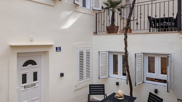Ein Innenhof mit einer Holzzugpergola, Blumentöpfen, einem Tisch mit Stühlen und einer Tür mit der Nummer 11.
