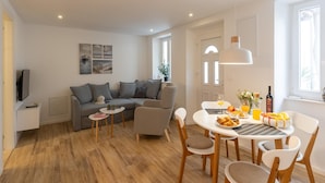 Ein modernes Wohnzimmer mit einer Couch, einem Esstisch mit Stühlen und einem Fernseher auf einem Lowboard.
