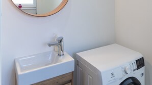 Ein kleines Badezimmer mit rundem Spiegel, weißem Waschbecken und einer Frontlader-Waschmaschine.