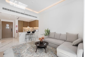 A modern living room with a sofa, a coffee table, and a kitchen area in the background. - Stayshort - Sophisticated Apartment in Meydan That Sleeps 4 (Dubai)