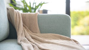 Un plaid beige en tricot est posé sur un canapé vert clair.