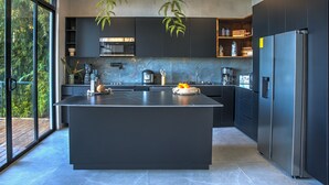 Une cuisine moderne dotée d’un grand îlot central, d’appareils électroménagers intégrés et d’un ventilateur de plafond.