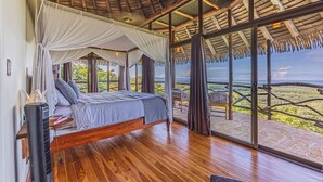 Une chambre avec un plancher en bois, un lit à baldaquin et une grande fenêtre donnant sur un paysage.