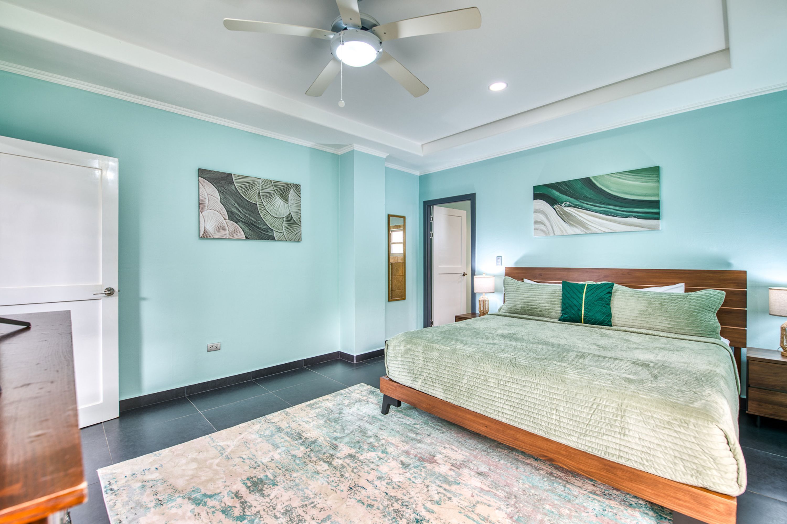 A bedroom with a bed, a ceiling fan, artwork on the walls, and a door.