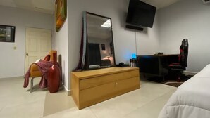 A bedroom with a bed, a dresser, a desk with a computer, a chair, a TV, and a door.
