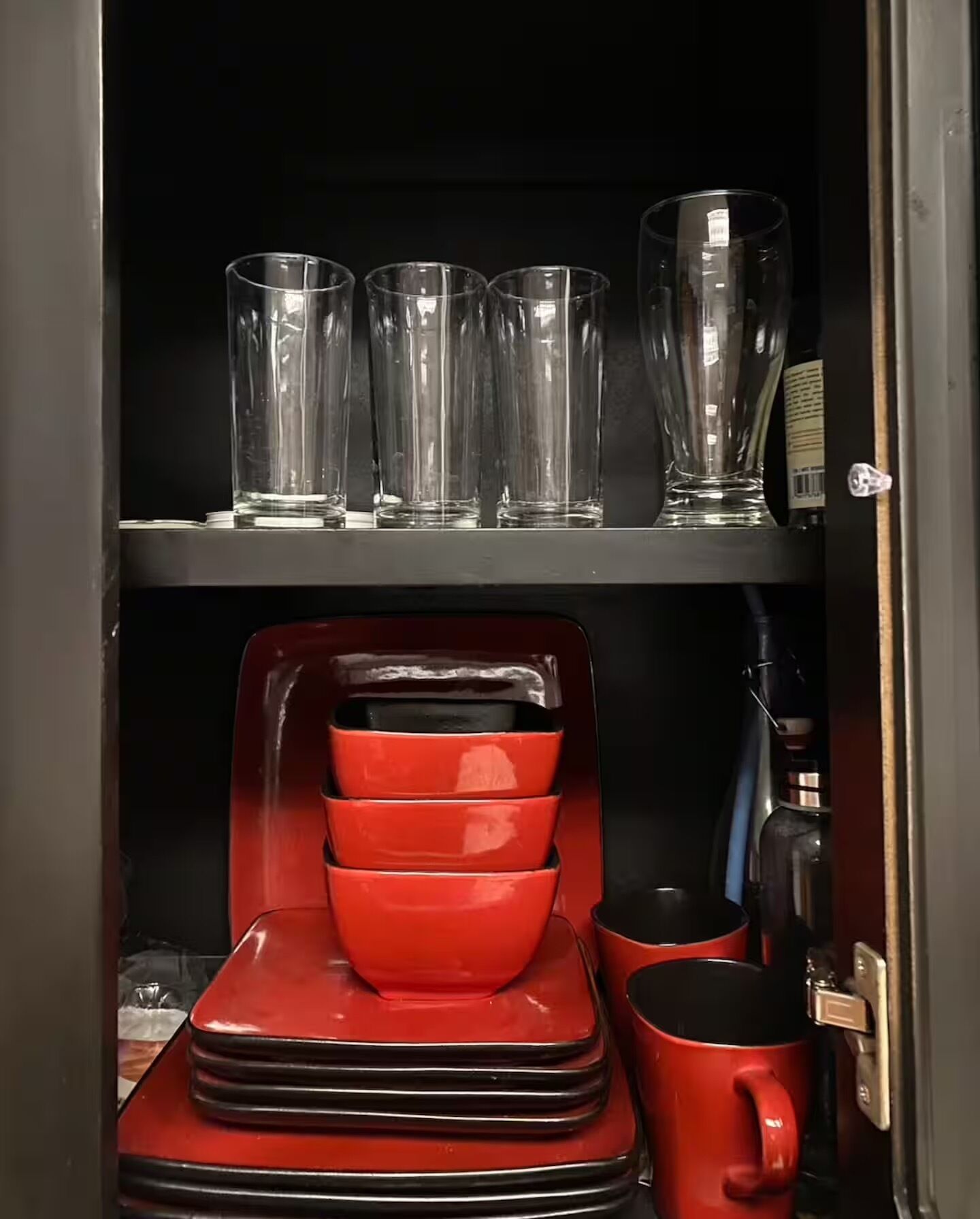 Un meuble de cuisine avec de la verrerie transparente sur l’étagère supérieure et des ustensiles de cuisine rouges sur l’étagère inférieure.