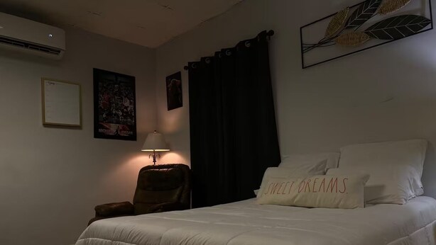 A hotel room with a bed, a desk, a chair, a lamp, and a wall with artwork.